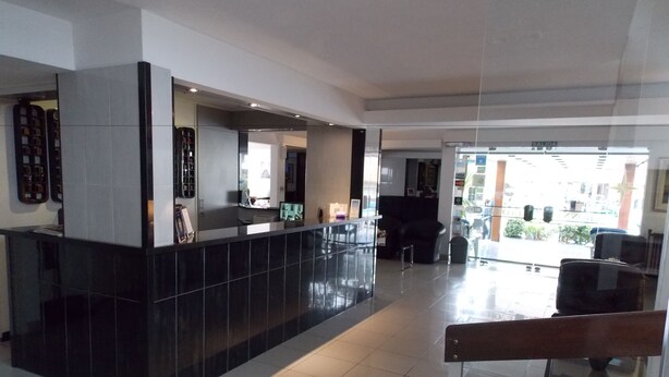 A modern reception area with a black reception desk, a seating area with a black sofa, and a glass partition. - Bonne Etoile Hotel (Punta del Este)