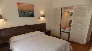 A bedroom with a bed, a nightstand, a lamp, a painting, and a wardrobe. - Bonne Etoile Hotel (Punta del Este)