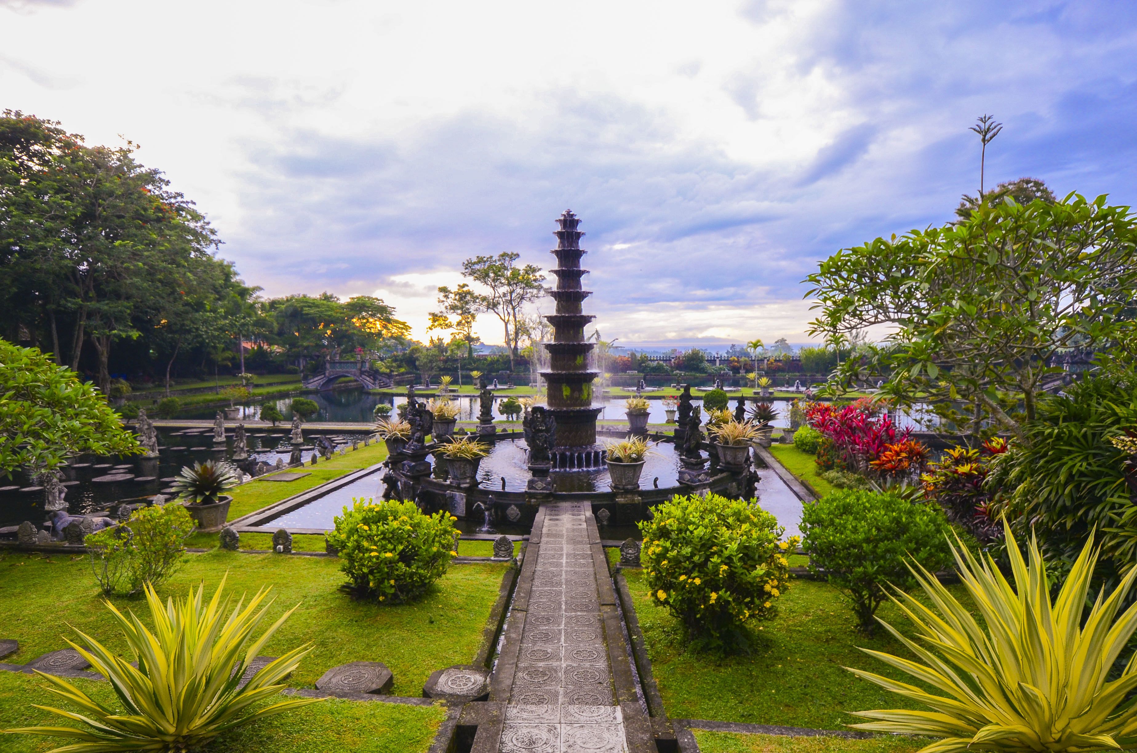 A traditional multi-tiered water fountain surrounded by lush greenery and a well-maintained garden.