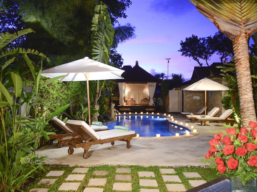 A pool area with lounge chairs and umbrellas, surrounded by tropical plants and a gazebo.