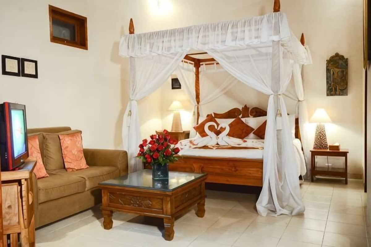 A bedroom with a four-poster bed, a wooden nightstand, a bedside table with a lamp, and a television on a wooden stand.