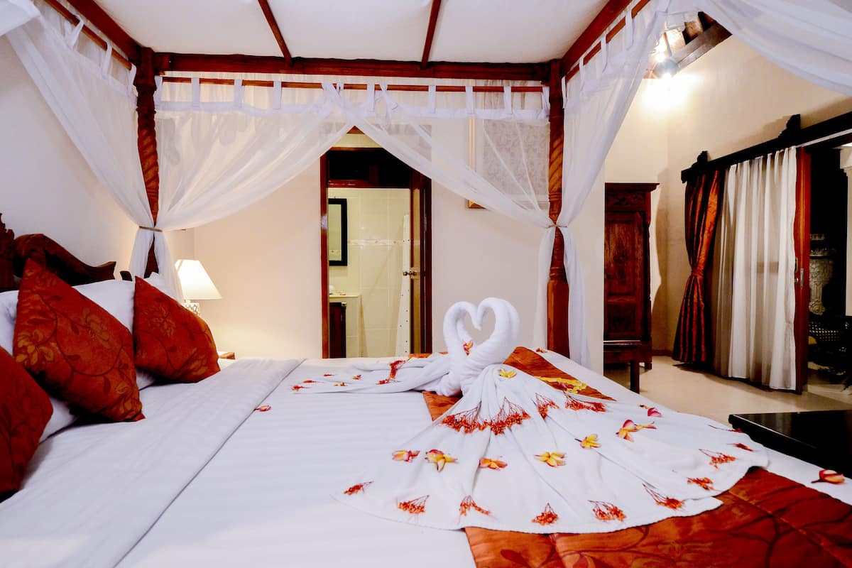 A neatly made bed with a floral bedspread, red pillows, and a white canopy.