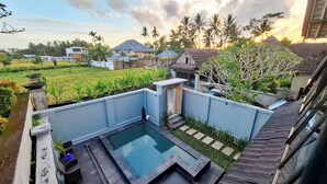 A swimming pool with a stone border, surrounded by a blue wall and a small garden area. - Villa Puri Darma Agung (Ubud)