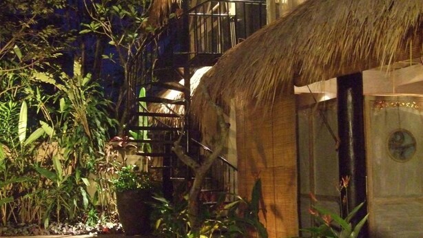 A building with a thatched roof and large windows, surrounded by tropical plants. - Villa Puri Darma Agung (Ubud)