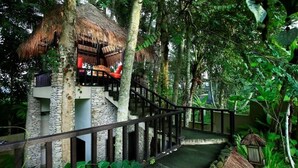 A treehouse with a thatched roof, stone walls, and a wooden staircase. - Villa Puri Darma Agung (Ubud)