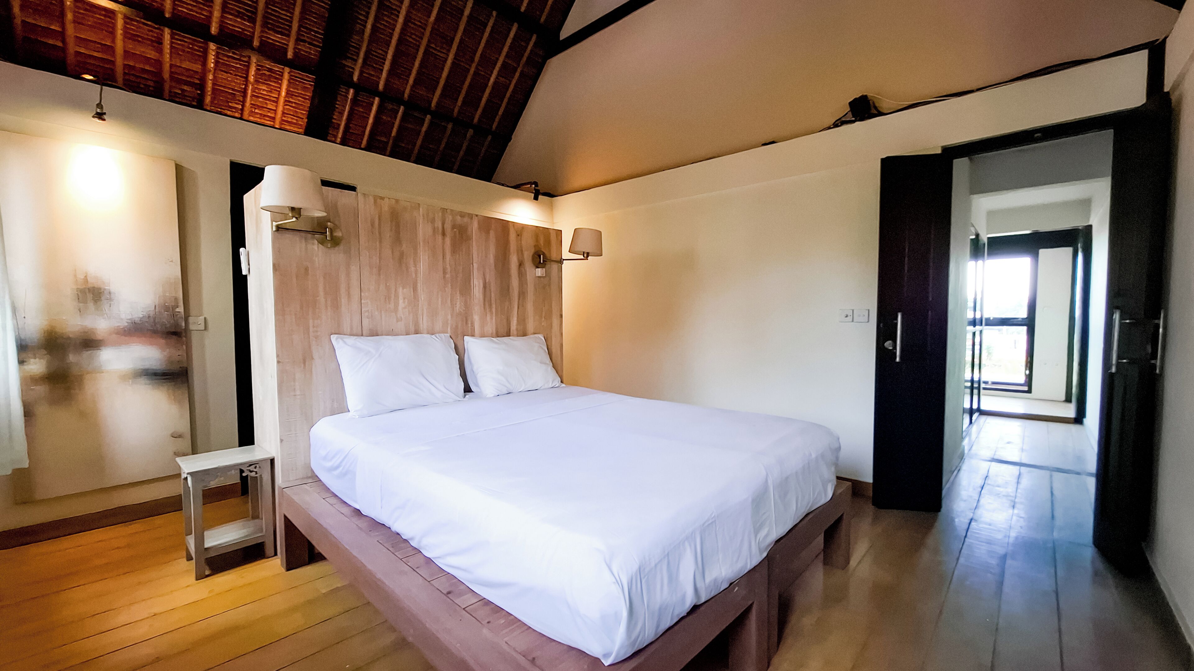 A bedroom with a wooden bed frame, white bedding, a nightstand, and two wall-mounted lamps.