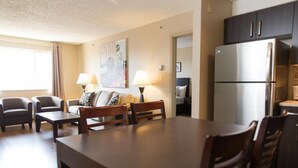 A modern living room with a dining table, two armchairs, a sofa, and a large painting on the wall. - Capital Suites Yellowknife (Yellowknife)