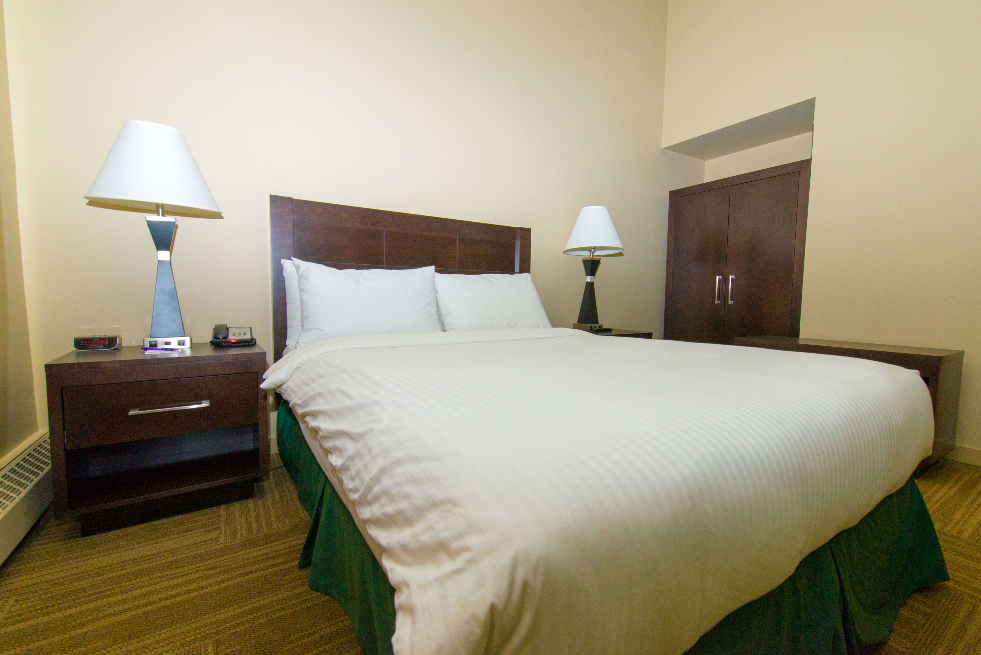 Habitación de hotel con una cama grande, dos mesitas de noche con lámparas, una mesita auxiliar y un armario.