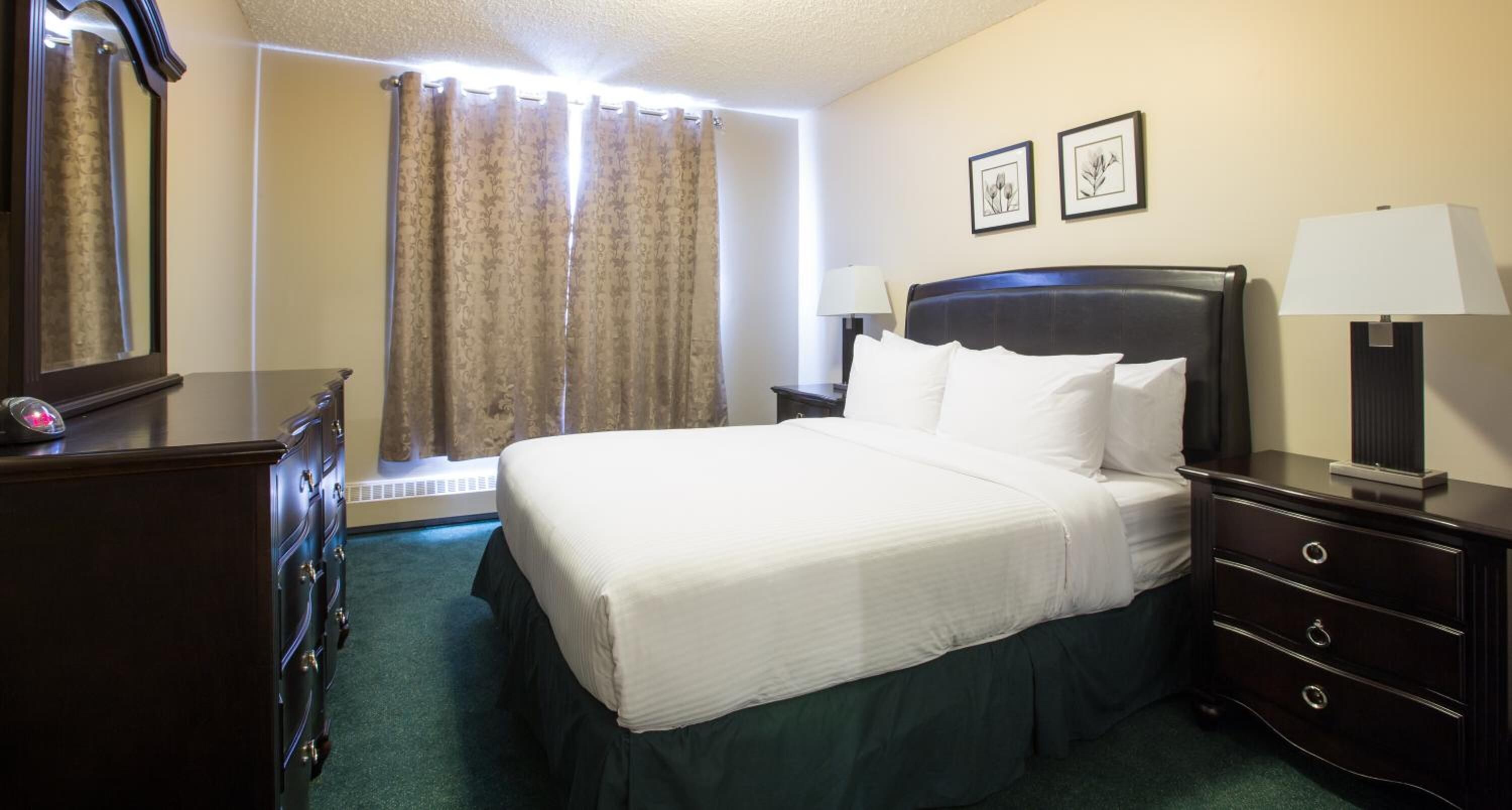 Una habitación de hotel con una cama grande, un tocador, una mesita de noche, una lámpara y dos cuadros en la pared.