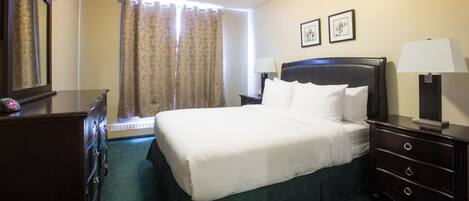 Una habitación de hotel con una cama grande, un tocador, una mesita de noche, una lámpara y dos cuadros en la pared.