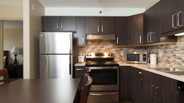 A modern kitchen with dark wood cabinets, stainless steel appliances, and a tiled backsplash. - Capital Suites Yellowknife (Yellowknife)