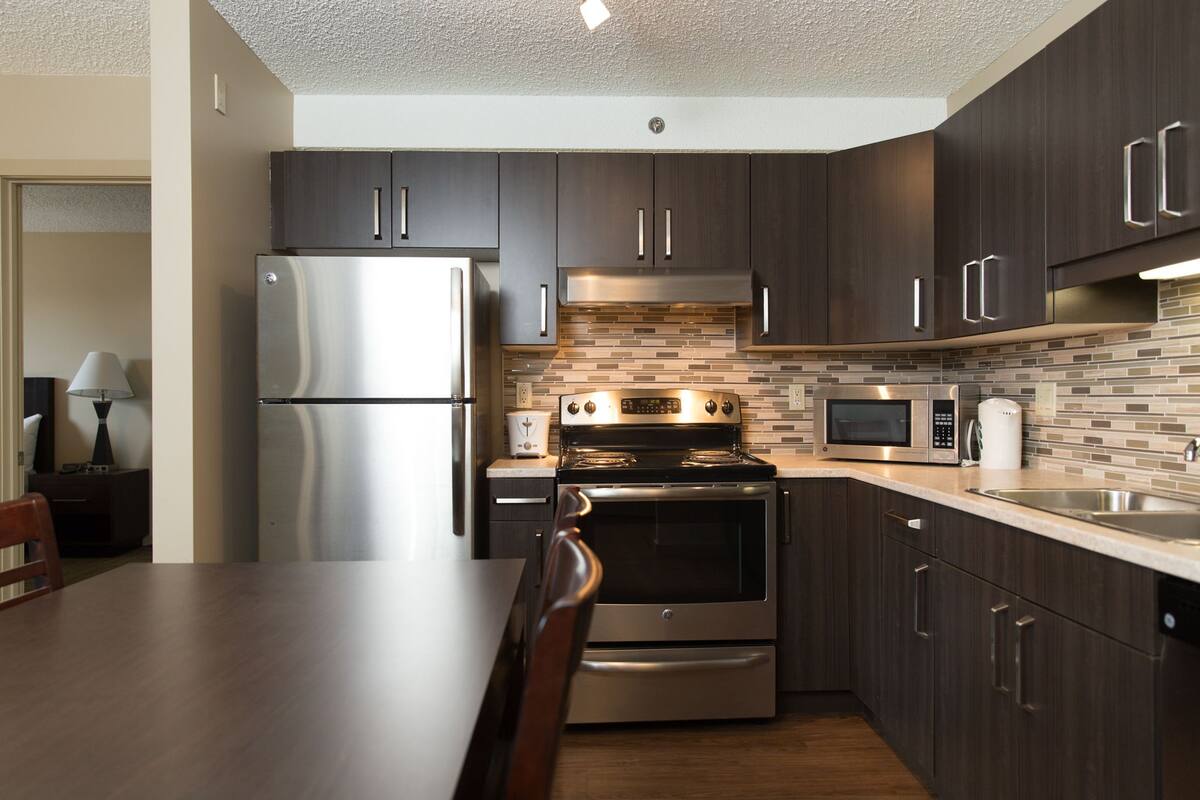 A modern kitchen with dark wood cabinets, stainless steel appliances, and a tiled backsplash.