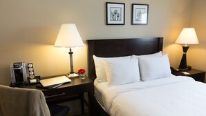 A hotel room with a bed, two bedside tables, a desk with a lamp, a chair, and a coffee maker. - Capital Suites Yellowknife (Yellowknife)
