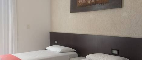 A hotel room with two beds, a red and white bedspread, a wall-mounted air conditioner, and a framed artwork above the beds.