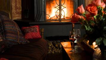 A cozy room with a fireplace, a sofa with patterned cushions, a table with wine glasses, and a vase with roses.