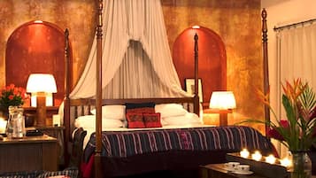 Una cama tradicional con dosel y cortinas, una mesita de noche con lámpara, y una mesilla con velas.