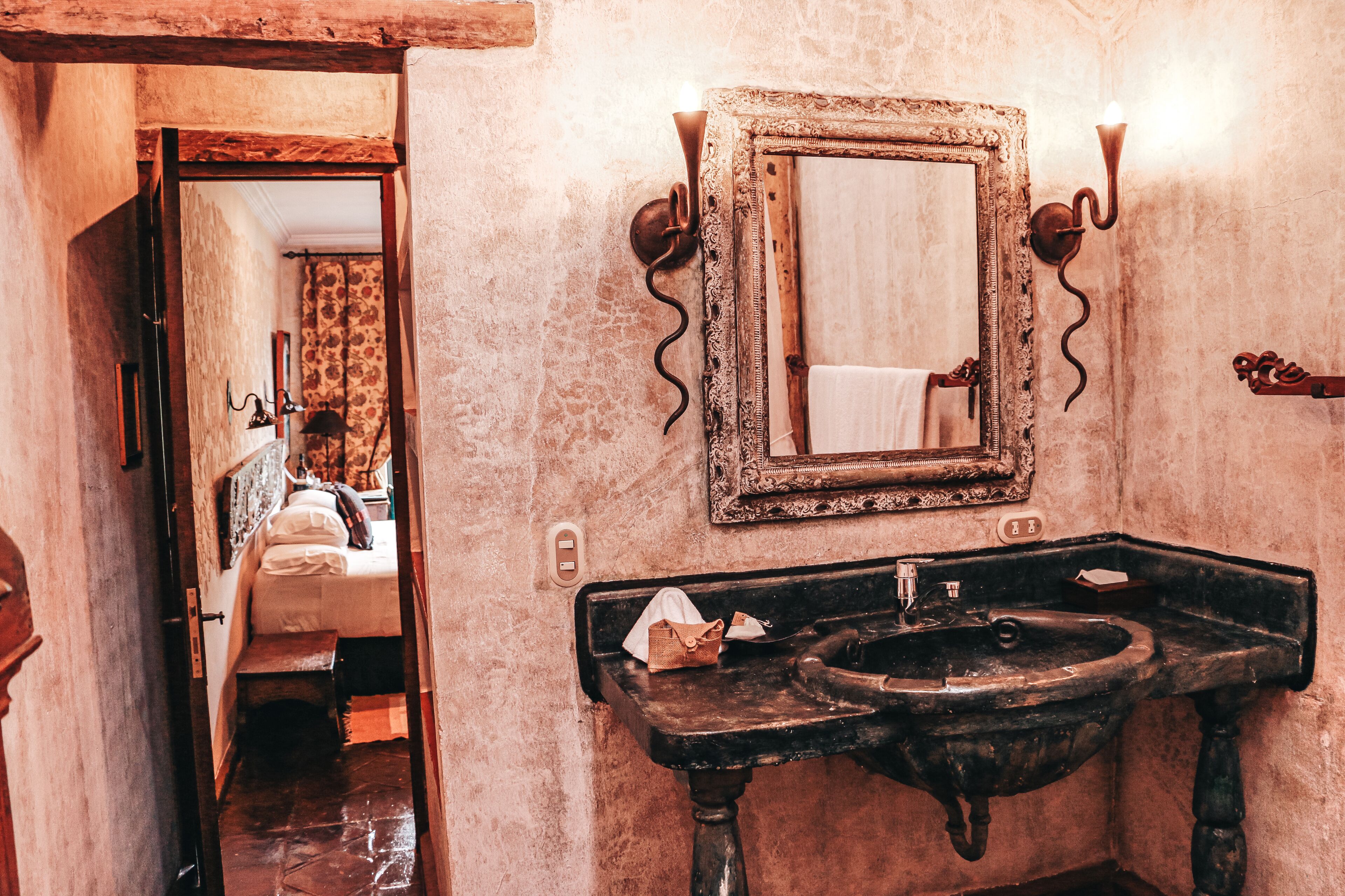 Ein Badezimmer im Vintage-Stil mit einem großen Spiegel, verzierten Wandleuchten und einem rustikalen Waschbecken.