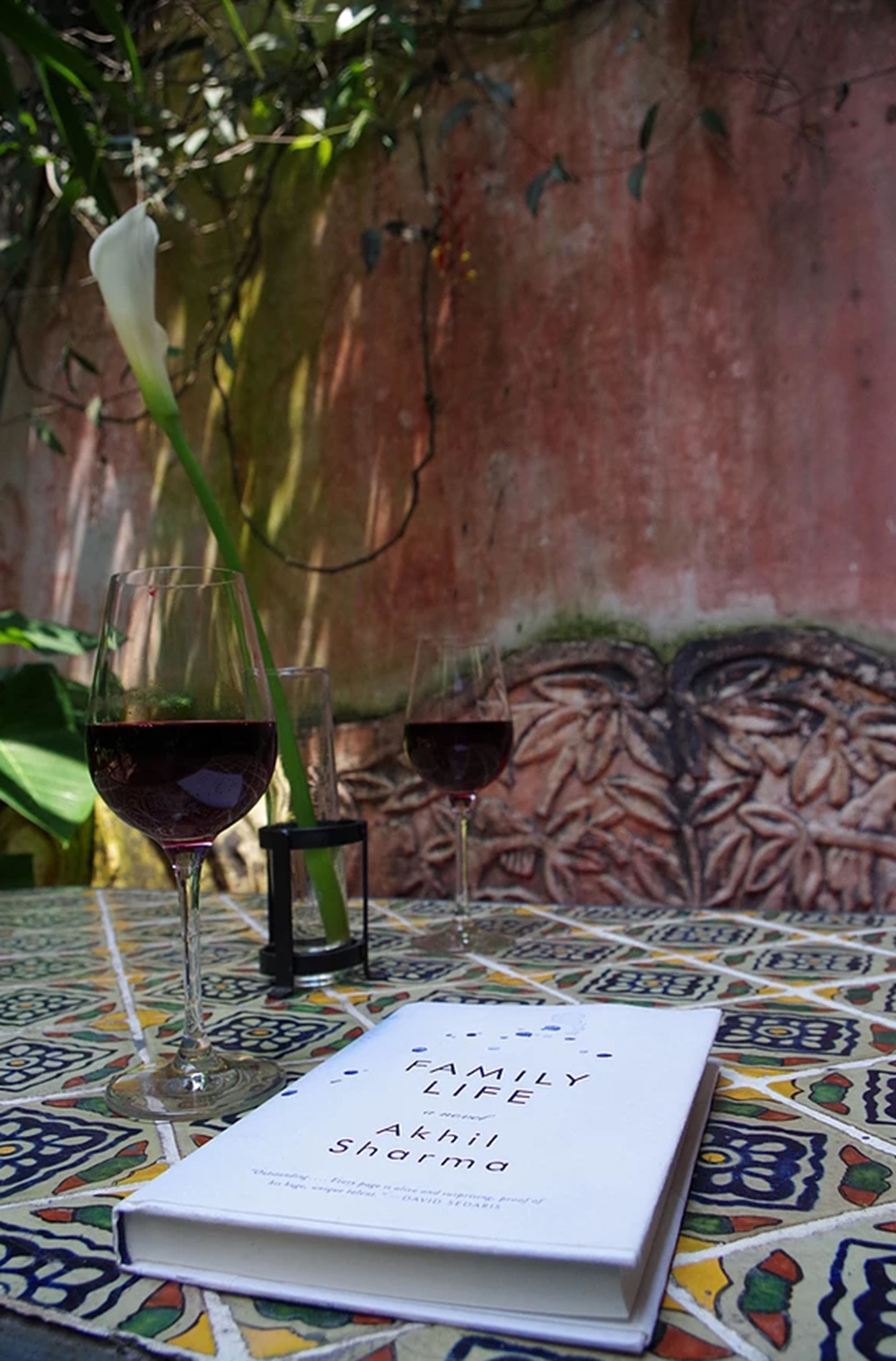 A book titled "Family Life" by Akhil Sharma on a tiled table with two wine glasses.