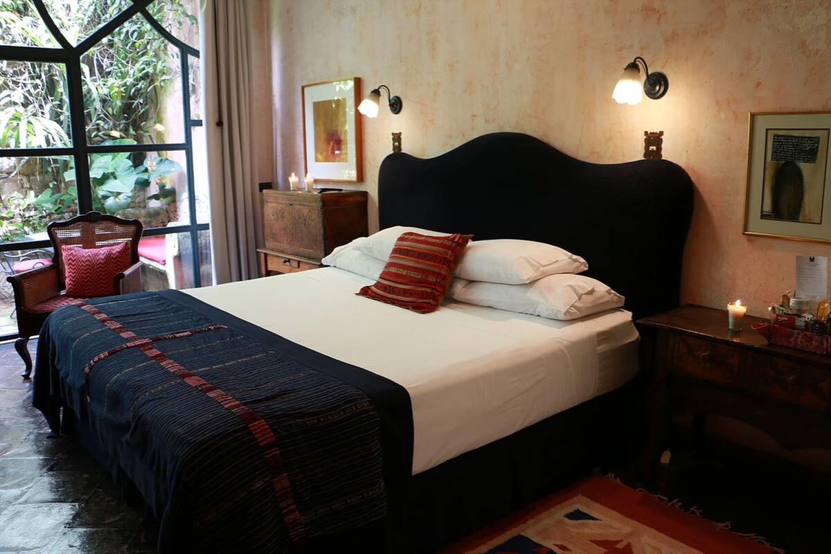 Une chambre à coucher avec un grand lit, une table de chevet, une chaise et une fenêtre donnant sur un paysage verdoyant.