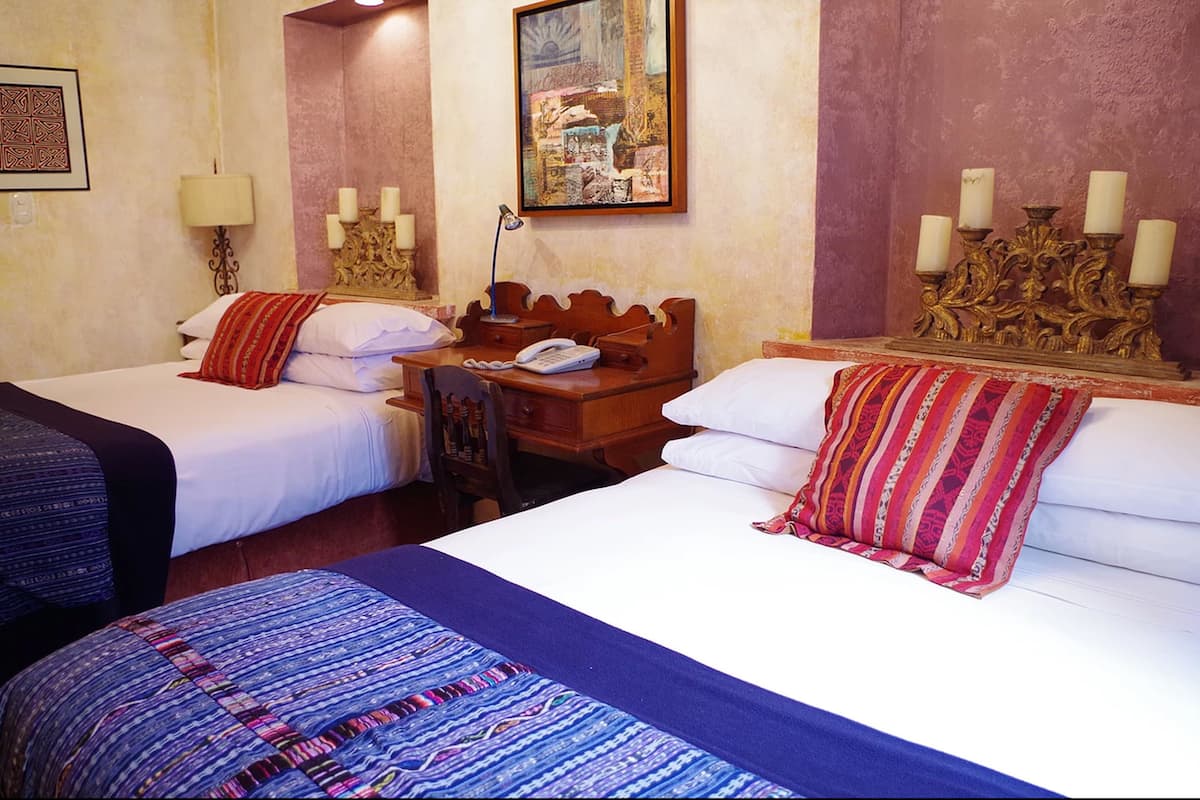 Une chambre d’hôtel avec deux lits, un bureau avec un téléphone et une lampe fixée au mur.