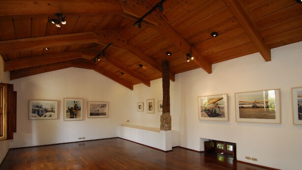 An art gallery with wooden beams, framed pictures on the walls, and a wooden floor. - Meson Panza Verde (Antigua Guatemala)