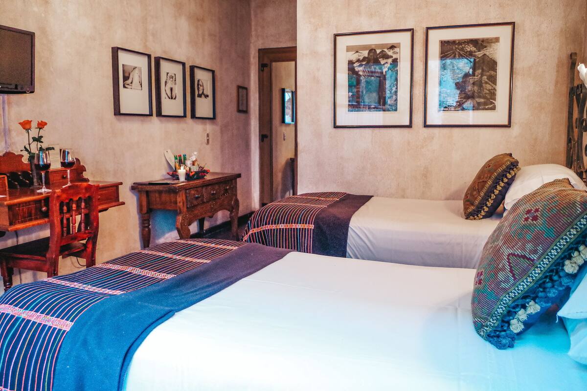 Une chambre d’hôtel avec deux lits, un bureau en bois et des tableaux encadrés accrochés au mur.