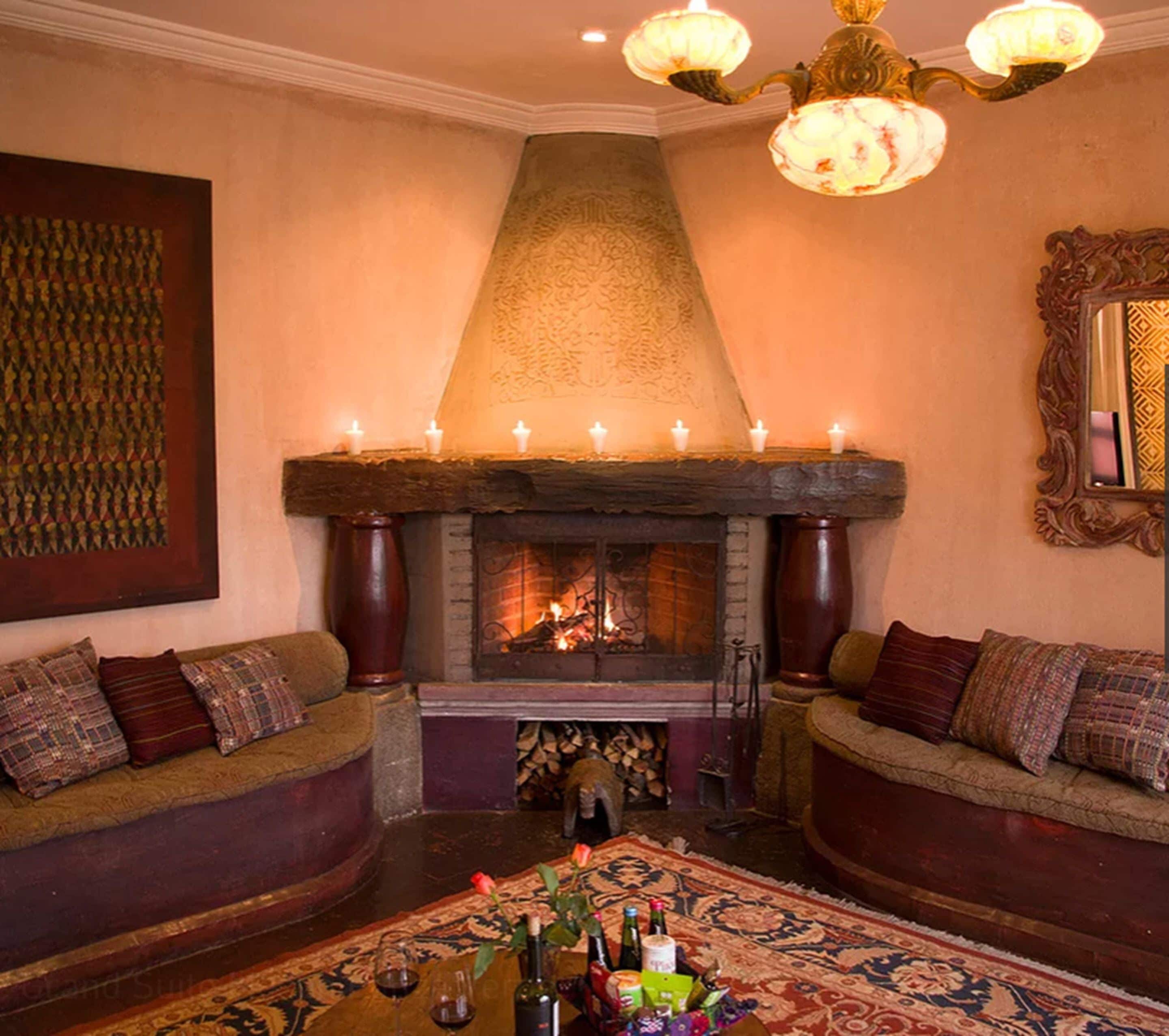 A cozy room with a fireplace, two sofas, a coffee table with drinks, and a chandelier.