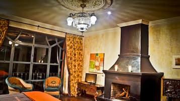 Una habitación con un ventanal grande, una chimenea, sillas de mimbre y un candelabro.