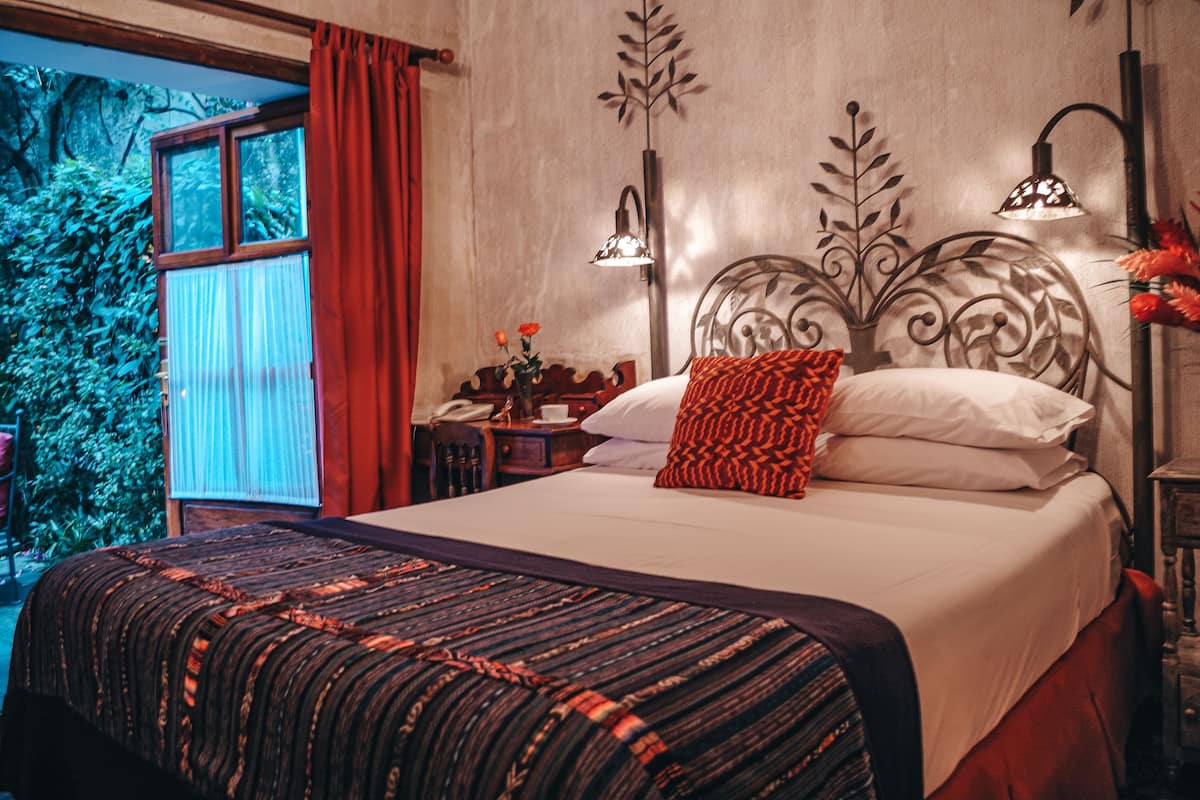 Un lit bien fait, avec une couvre-lit à motifs, une tête de lit décorative et deux lampes de chevet.