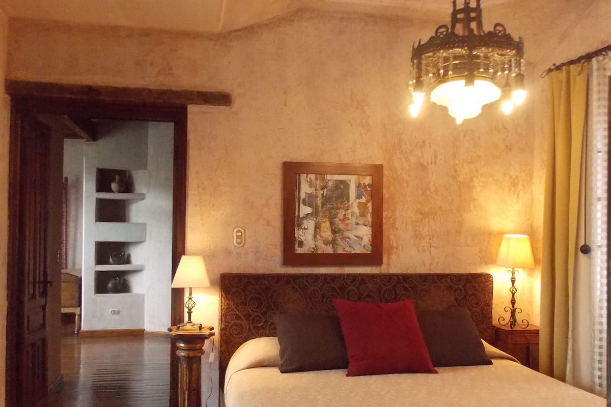 Une chambre spacieuse avec un grand lit, un lustre et deux lampes de chevet.