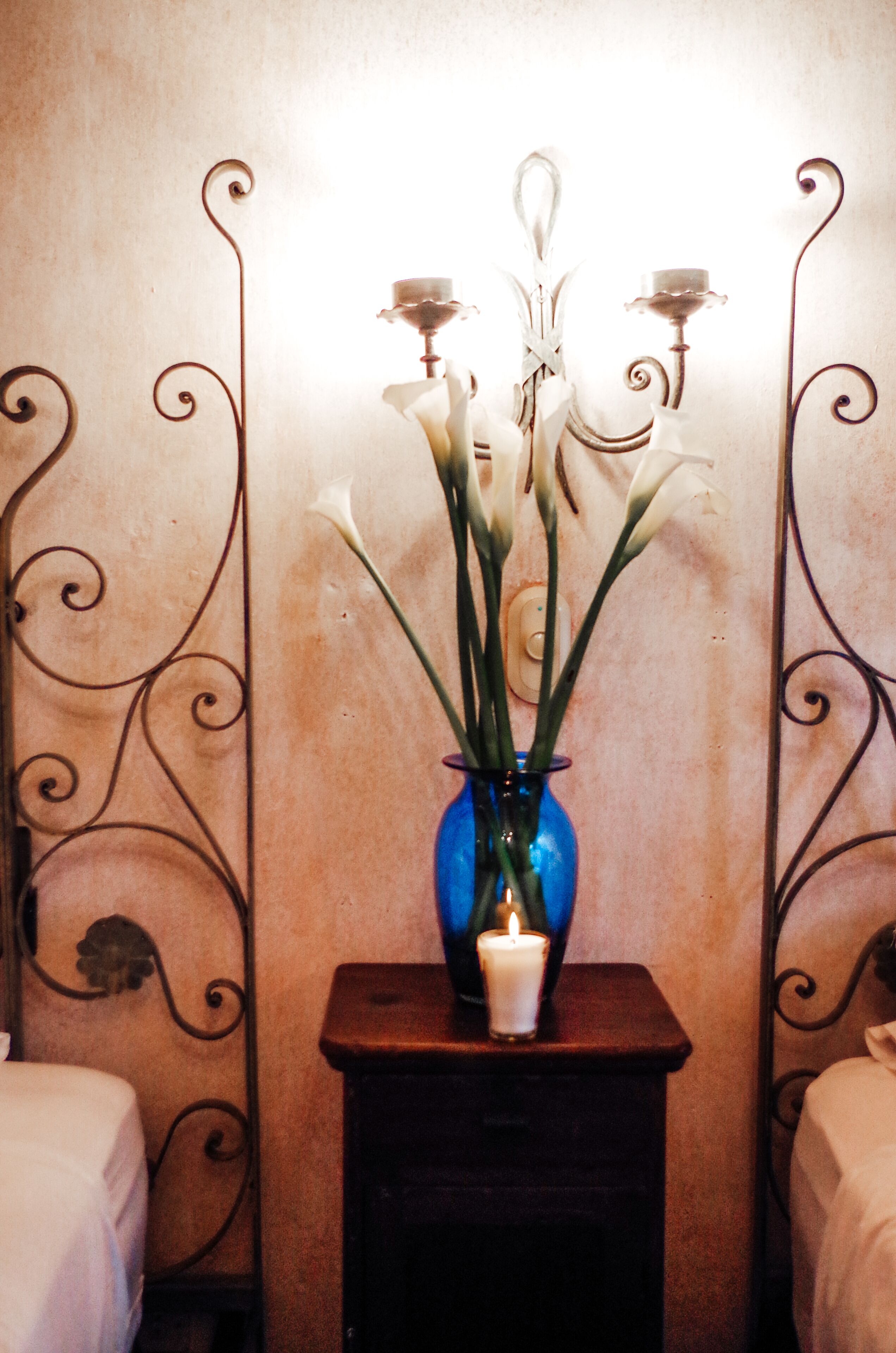 A blue vase with white flowers and candles on a bedside table in a room with metal bed frames.