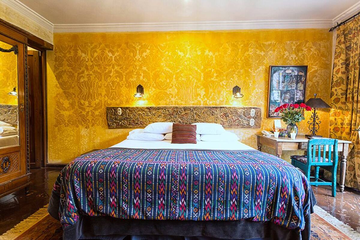 Une chambre d’hôtel avec un grand lit, une tête de lit en bois, deux lampes de chevet, une table de chevet ornée d’un vase de fleurs et un fauteuil.