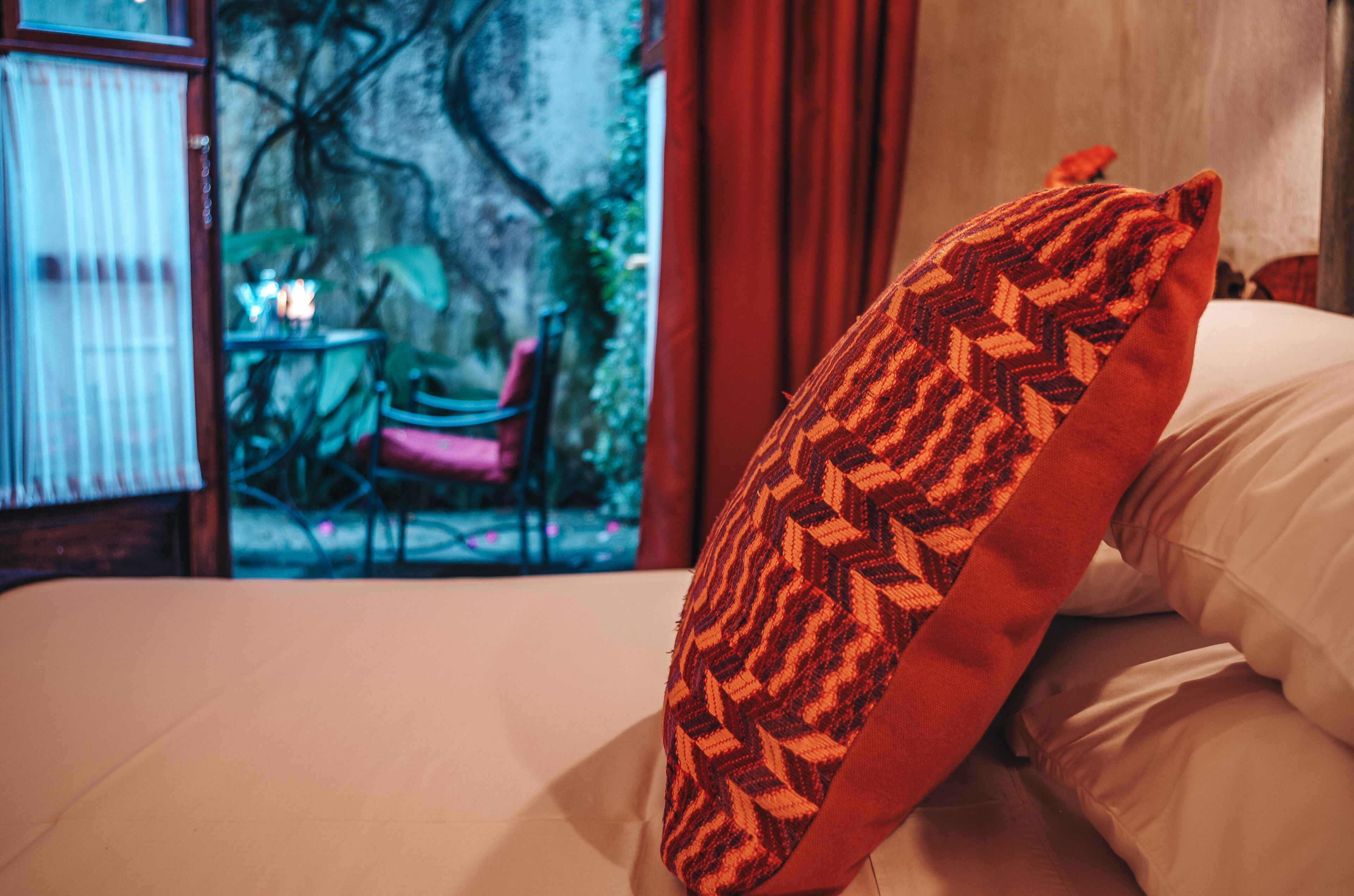 A bed with a patterned pillow and a view of an outdoor seating area with a table and chairs.