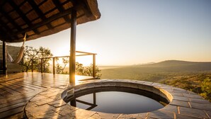 A hot tub with a stone surround, a hammock, and a wooden deck overlooking a valley.