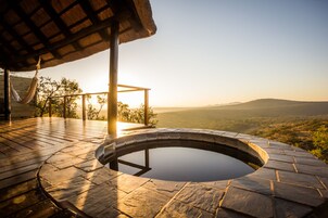 Un jacuzzi con revestimiento de piedra, una hamaca y una terraza de madera con vistas a un valle.