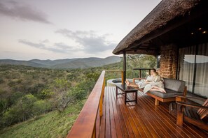 A wooden deck with a thatched roof, a sofa, and a table. - Leopard Mountain Safari Lodge (Jozini)