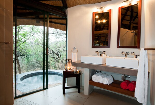 A bathroom with a large window, two sinks, a mirror, and a shelf with towels. - Leopard Mountain Safari Lodge (Jozini)