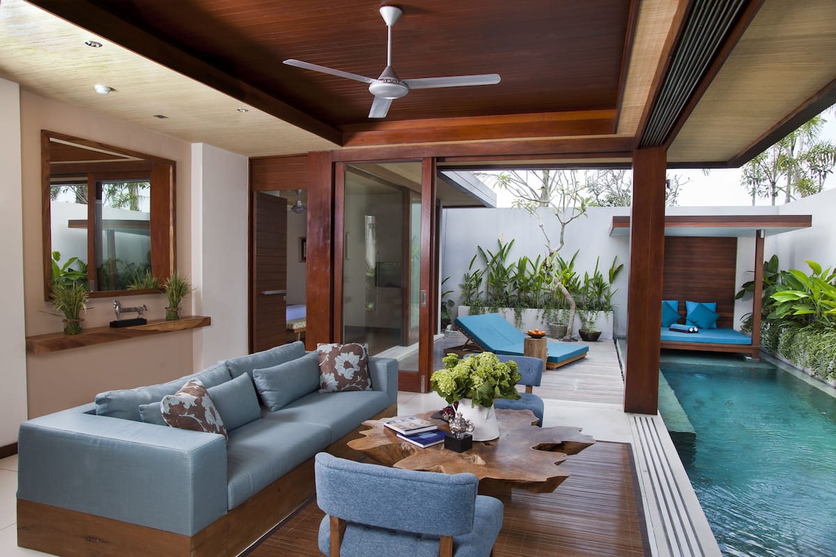Una sala de estar moderna con sofá, mesa de centro y vistas a una zona de piscina a través de puertas de vidrio.