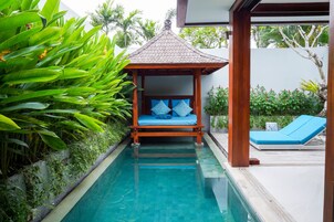 A poolside area with a wooden gazebo, a lounge chair, and lush greenery.