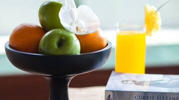 Uma mesa de madeira com uma tigela de frutas, um copo de suco de laranja e um livro chamado "American Table".