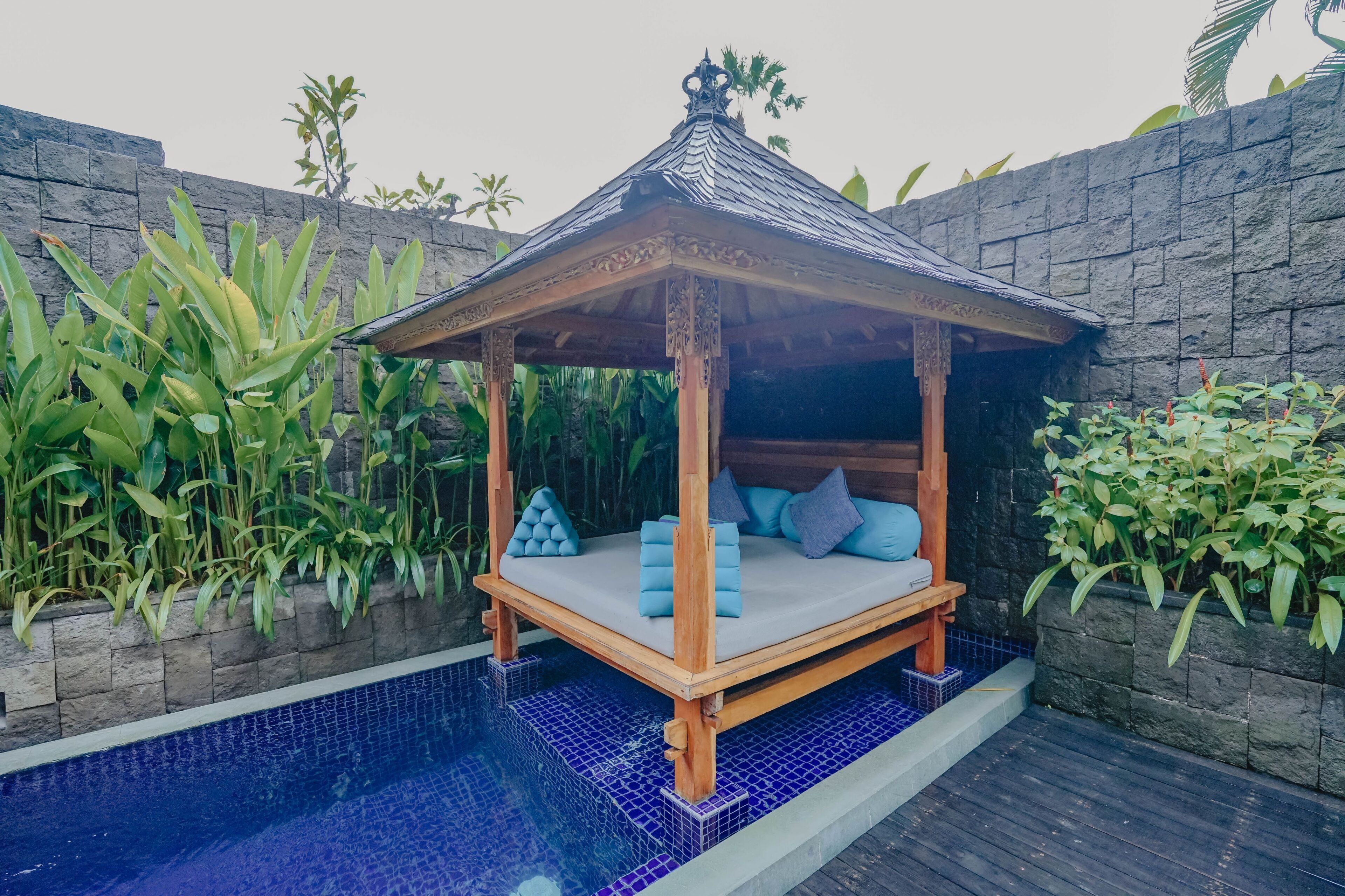 A wooden canopy bed with a tiled pool in the background.