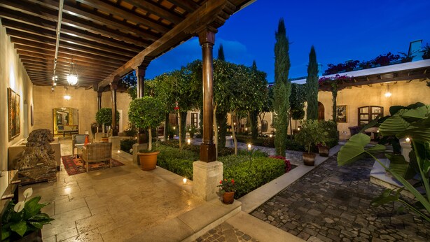 A covered outdoor area with stone flooring, potted plants, and a wooden pergola. - San Rafael Hotel (Antigua Guatemala)