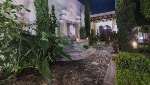 A courtyard with a stone pathway, a fountain, and a building with a white facade and blue accents. - San Rafael Hotel (Antigua Guatemala)