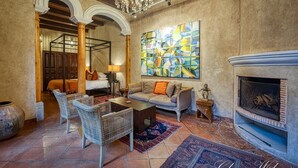 A cozy living room with a fireplace, a sofa, wicker chairs, and a colorful abstract painting on the wall. - San Rafael Hotel (Antigua Guatemala)