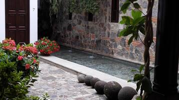 A courtyard with a stone pathway, a small water feature, and a building with a stone facade and a wooden door.