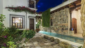 A courtyard with a swimming pool, stone walls, and a white building with a balcony. - San Rafael Hotel (Antigua Guatemala)