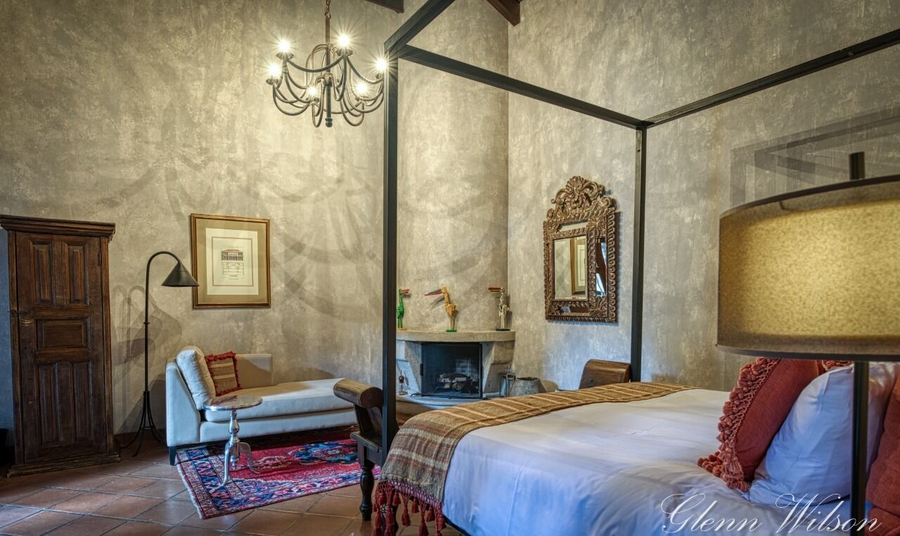 A bedroom with a four-poster bed, a chandelier, a fireplace, and a large mirror.