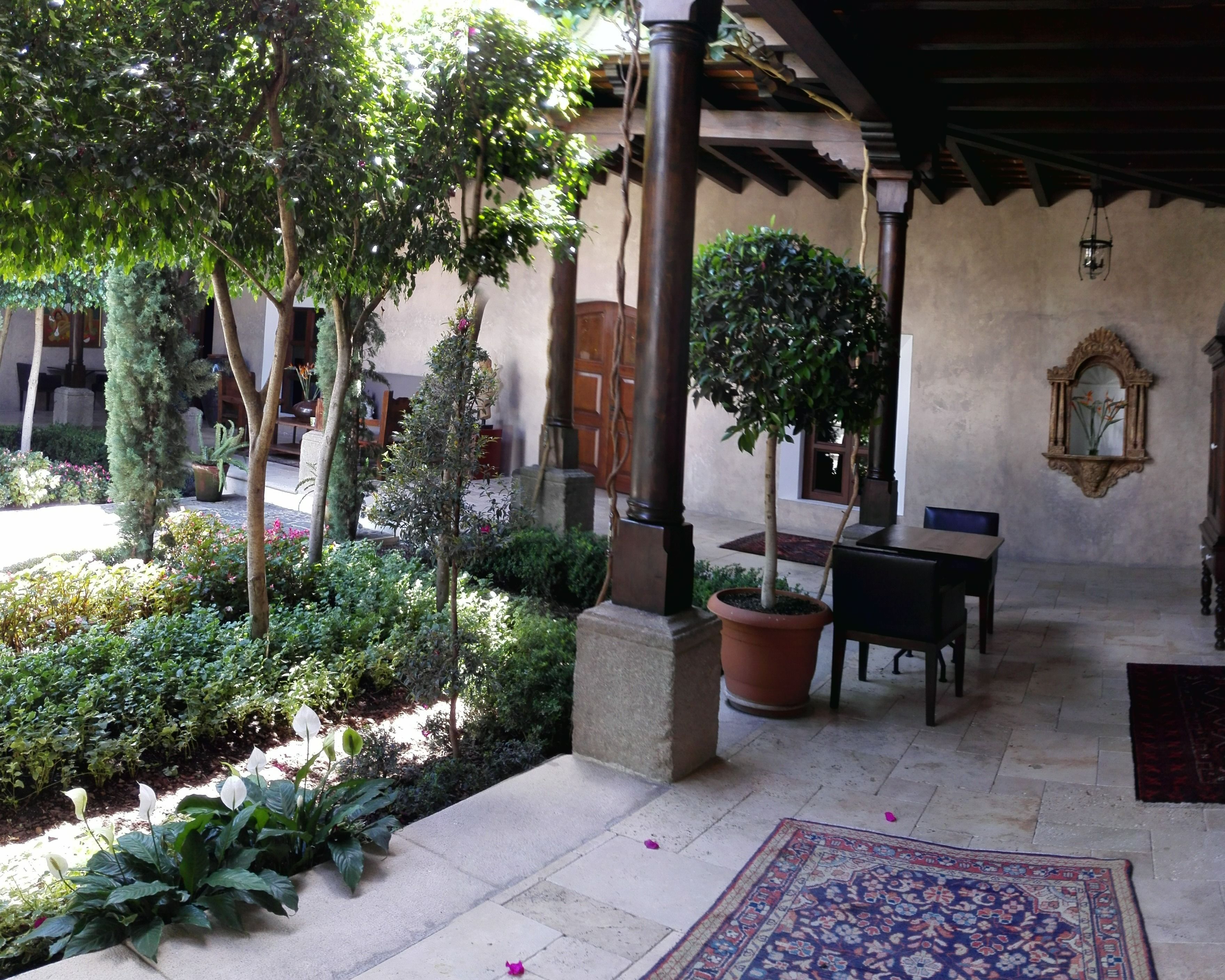A covered patio area with a tiled floor, potted plants, a table, and a chair.