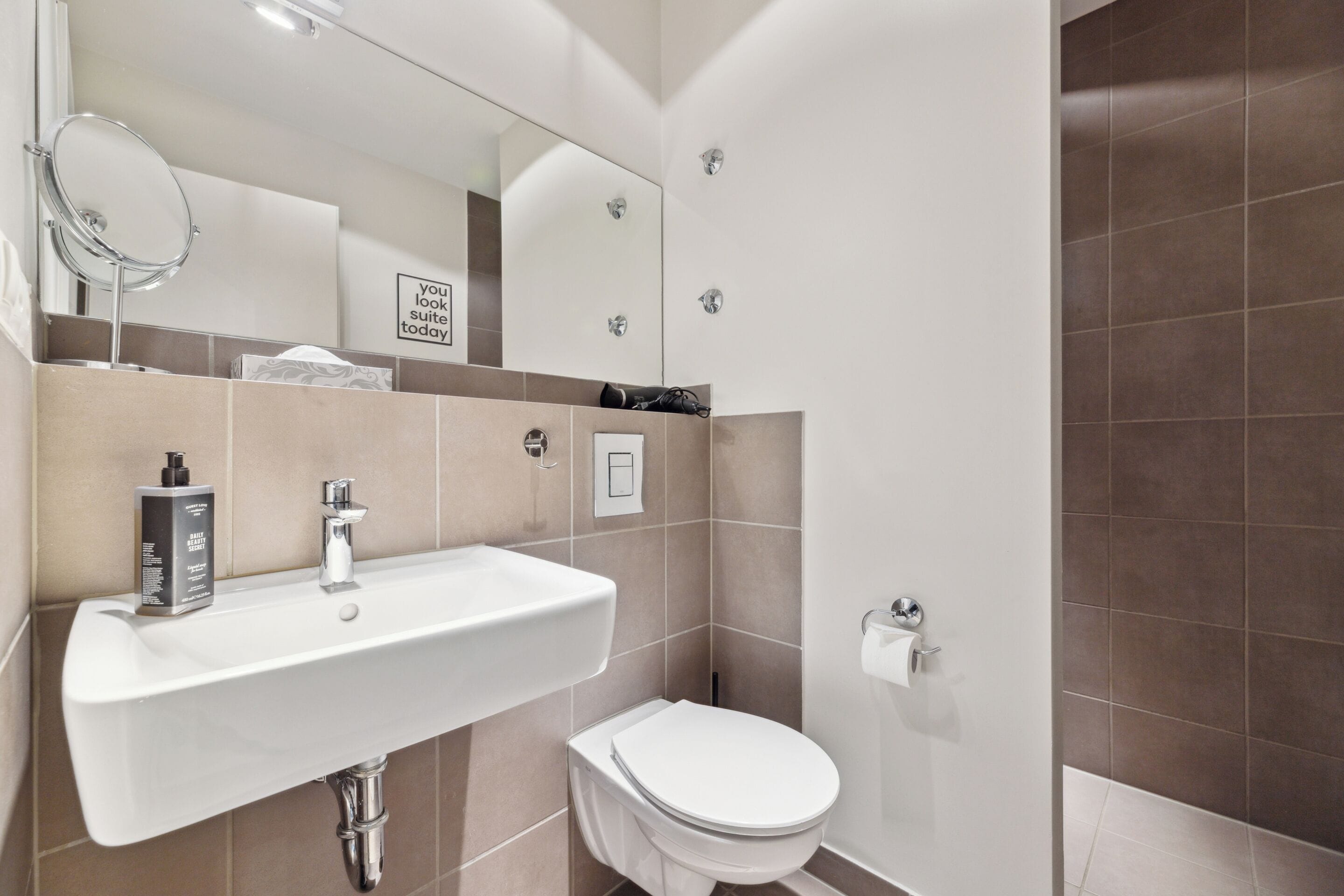 A modern bathroom with a white sink, mirror, and toilet.