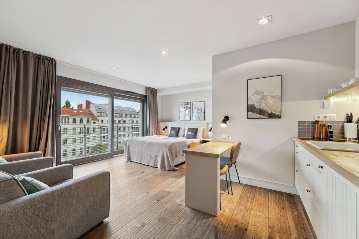 Une chambre d’hôtel moderne dotée d’une grande fenêtre, d’un lit, d’un bureau et d’une kitchenette.